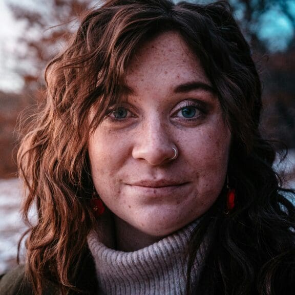 Woman with nose ring looking directly at camera. The woman is looking reflective. There is a wintery background.