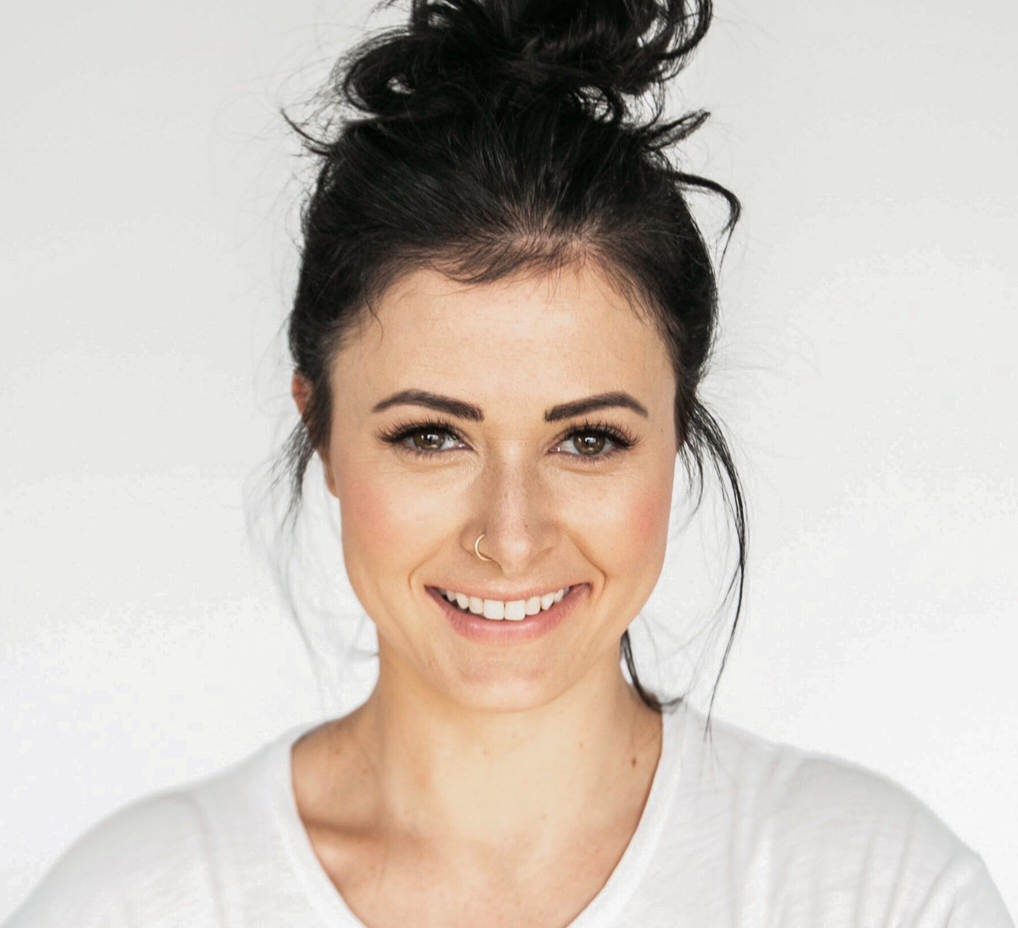 Young woman with black hair tied and nose ring smiling at camera