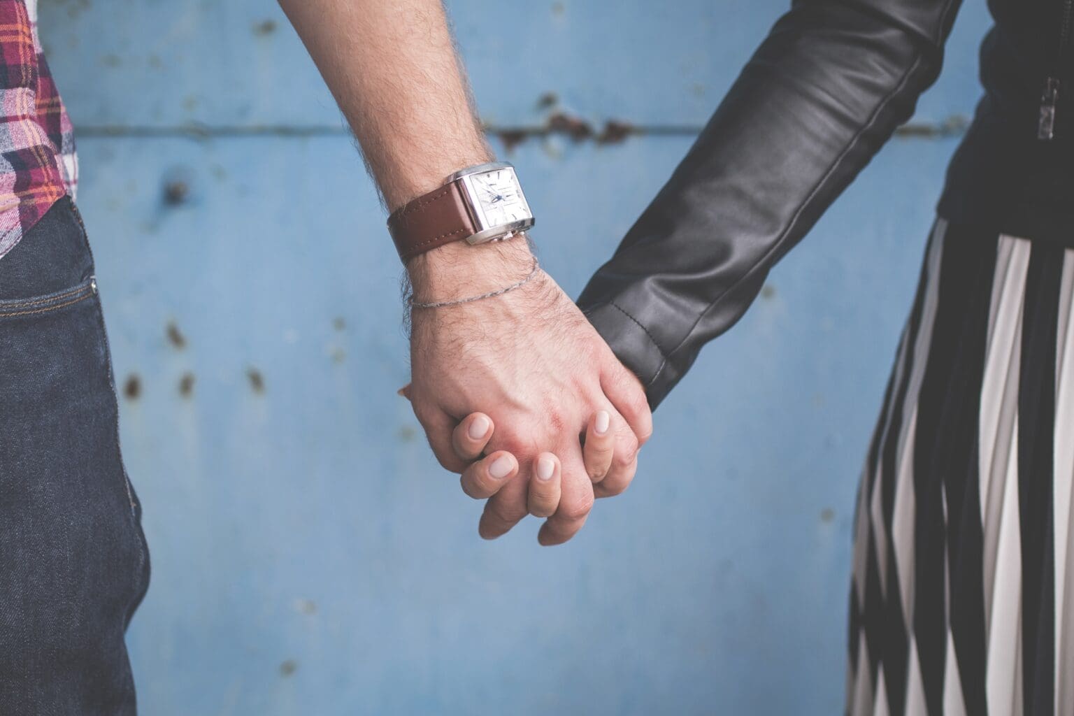 Male holding female hand. Hi wearing a watch. She is wearing a black leather jacket.