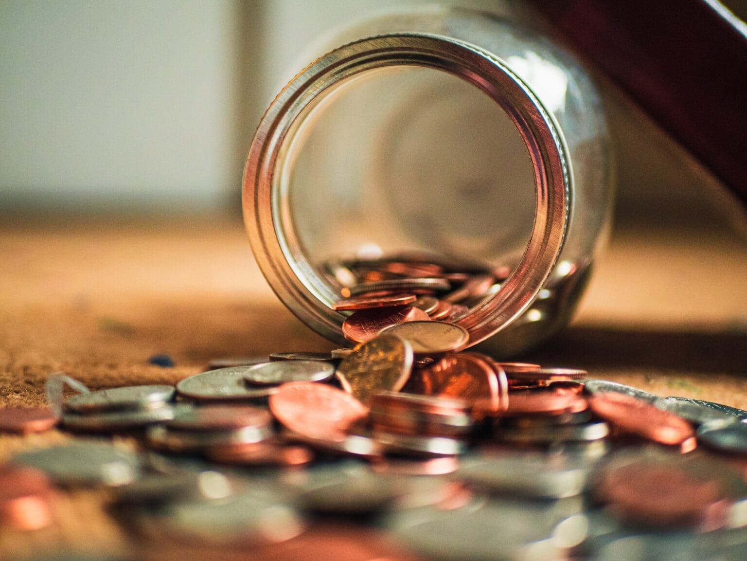 A jar of silver and bronze coins on its side on the floor with coins spilling out.