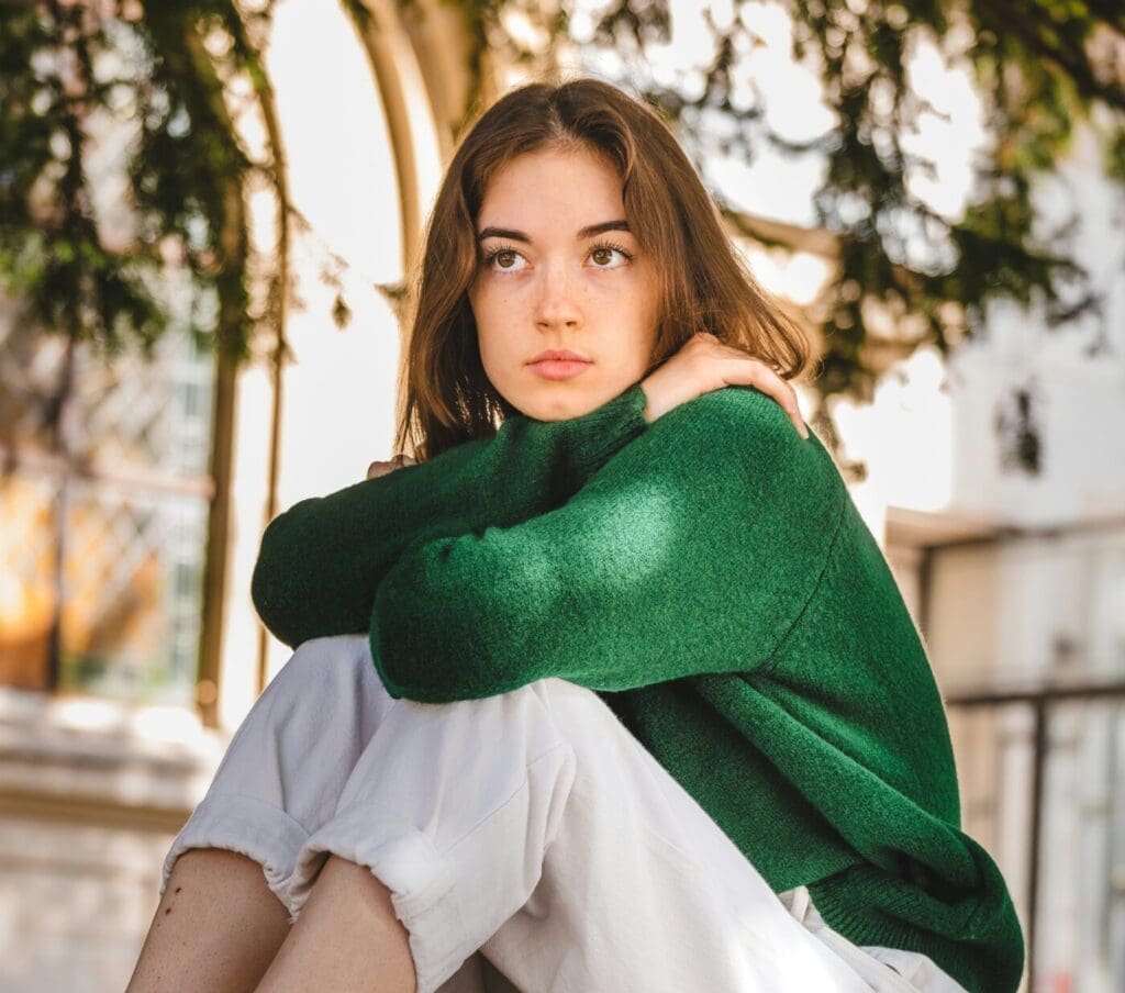 teenage girl with brown hair. She is sitting outside looking out into the distance.