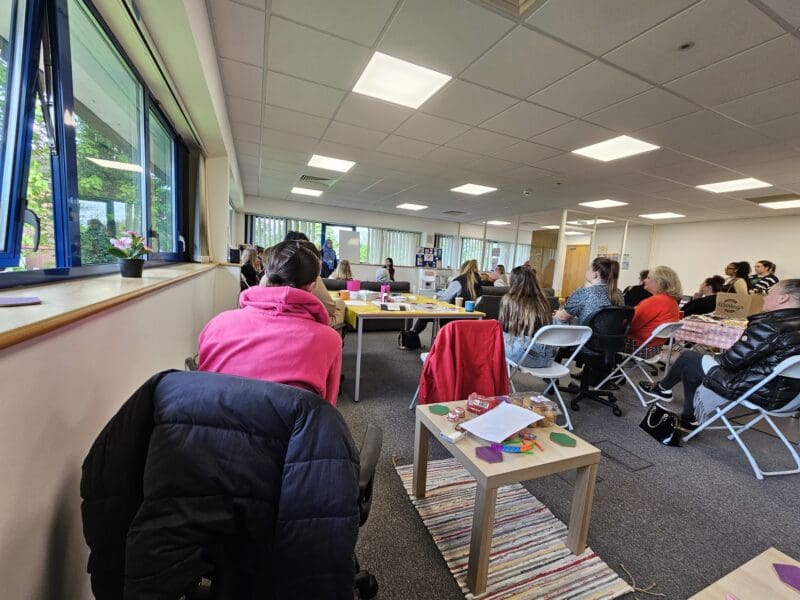 women gathered in a meeting room. Seated. Watching a presentation. Backs to camera
