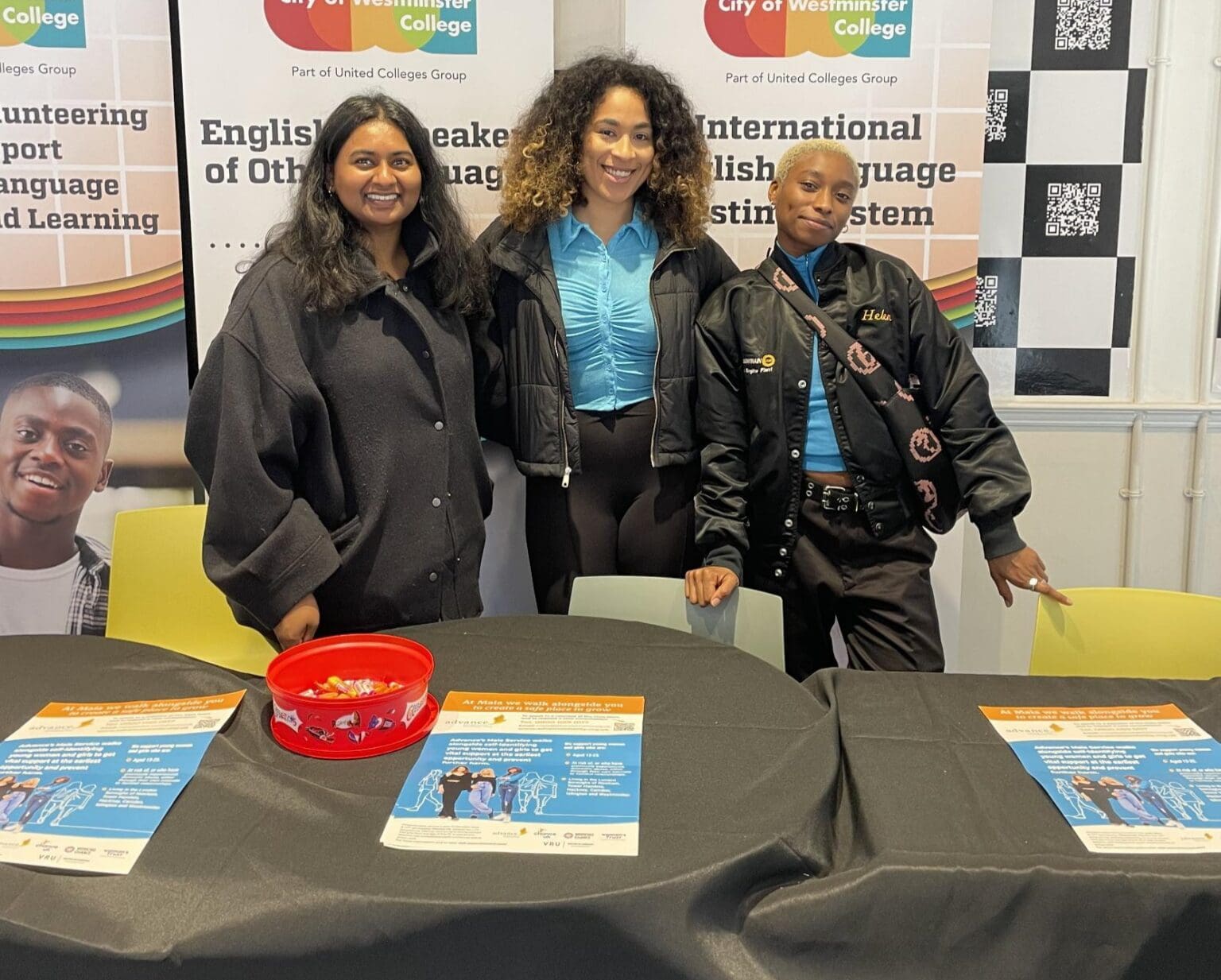 Three young women standing together behind a table covered in a black cloth.