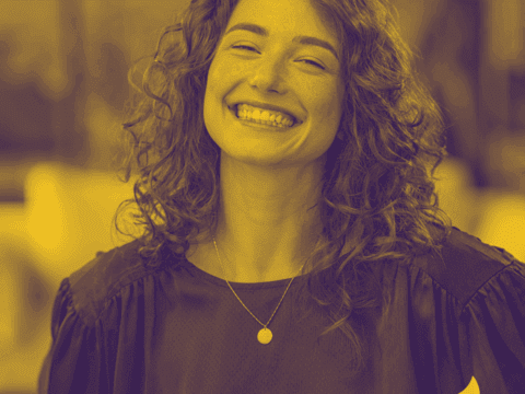 portrait of young woman laughing. She has curly hair and is looking directly at the camera. The image is in a yellow and purple duo tone.