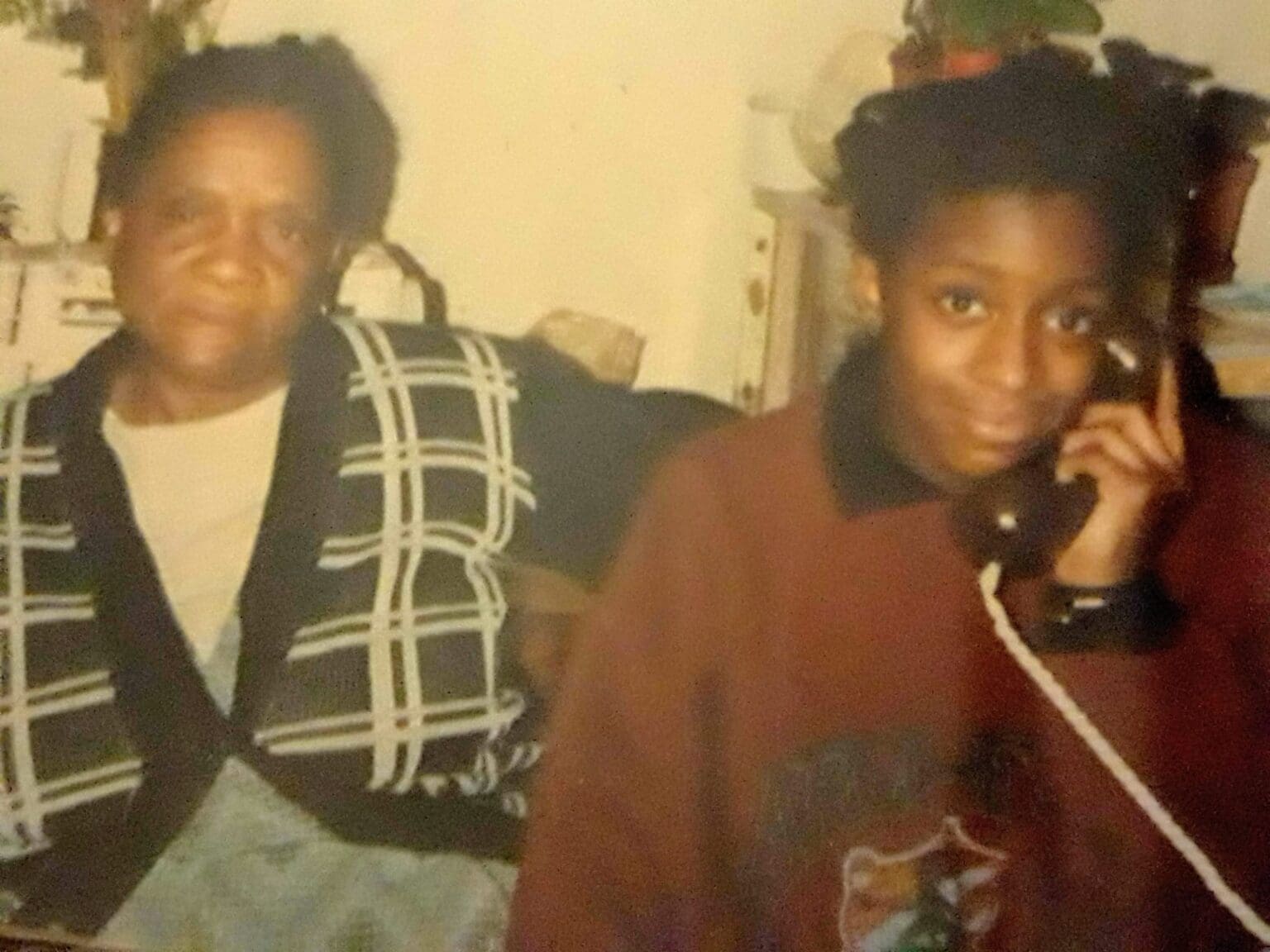 Woman sitting next to a teenage girl who is holding a corded phone to her ear.